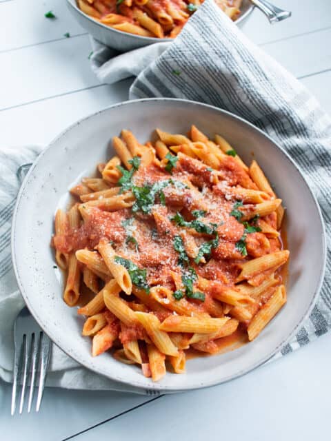 penne with vodka sauce in a white bowl on a gray towel