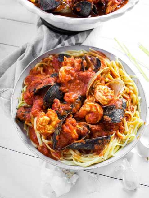 Seafood in a red sauce sitting on top of pasta in a white bowl