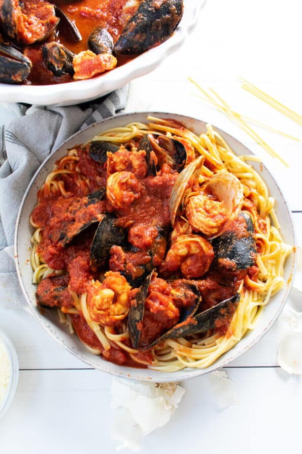 Seafood in a red sauce sitting on top of pasta in a white bowl