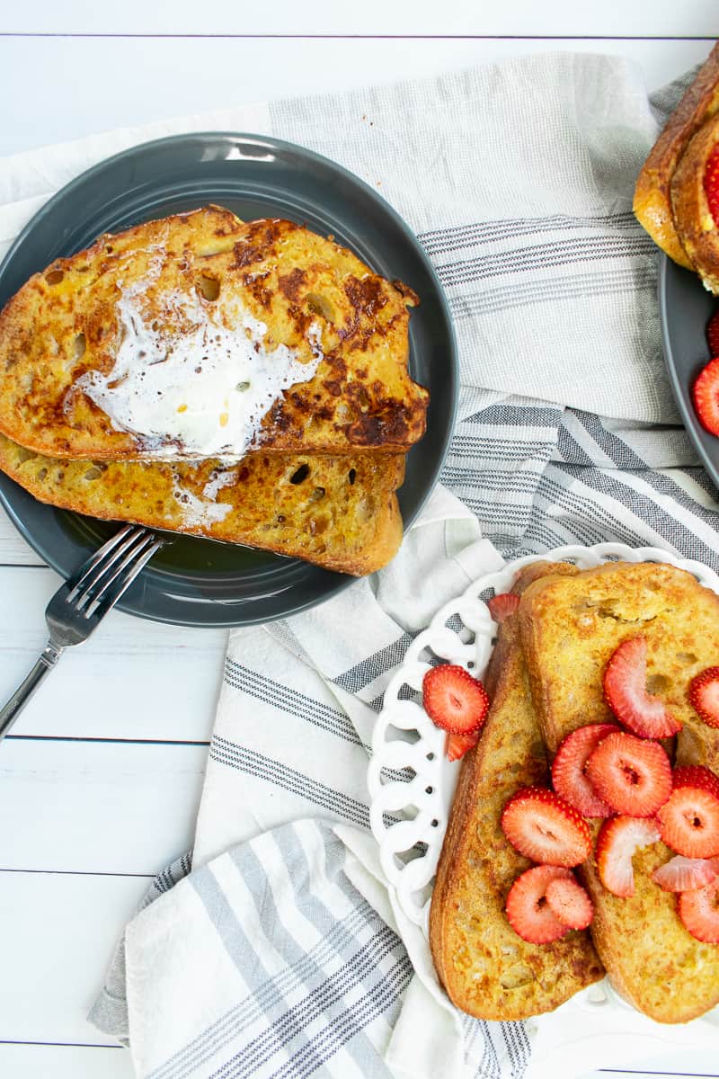 french toast slices on small plates with strawberries and white background