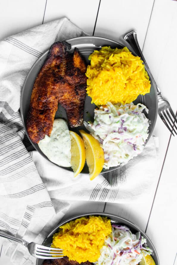 a plate of blackened fish, yellow rice, and cole slaw on white table
